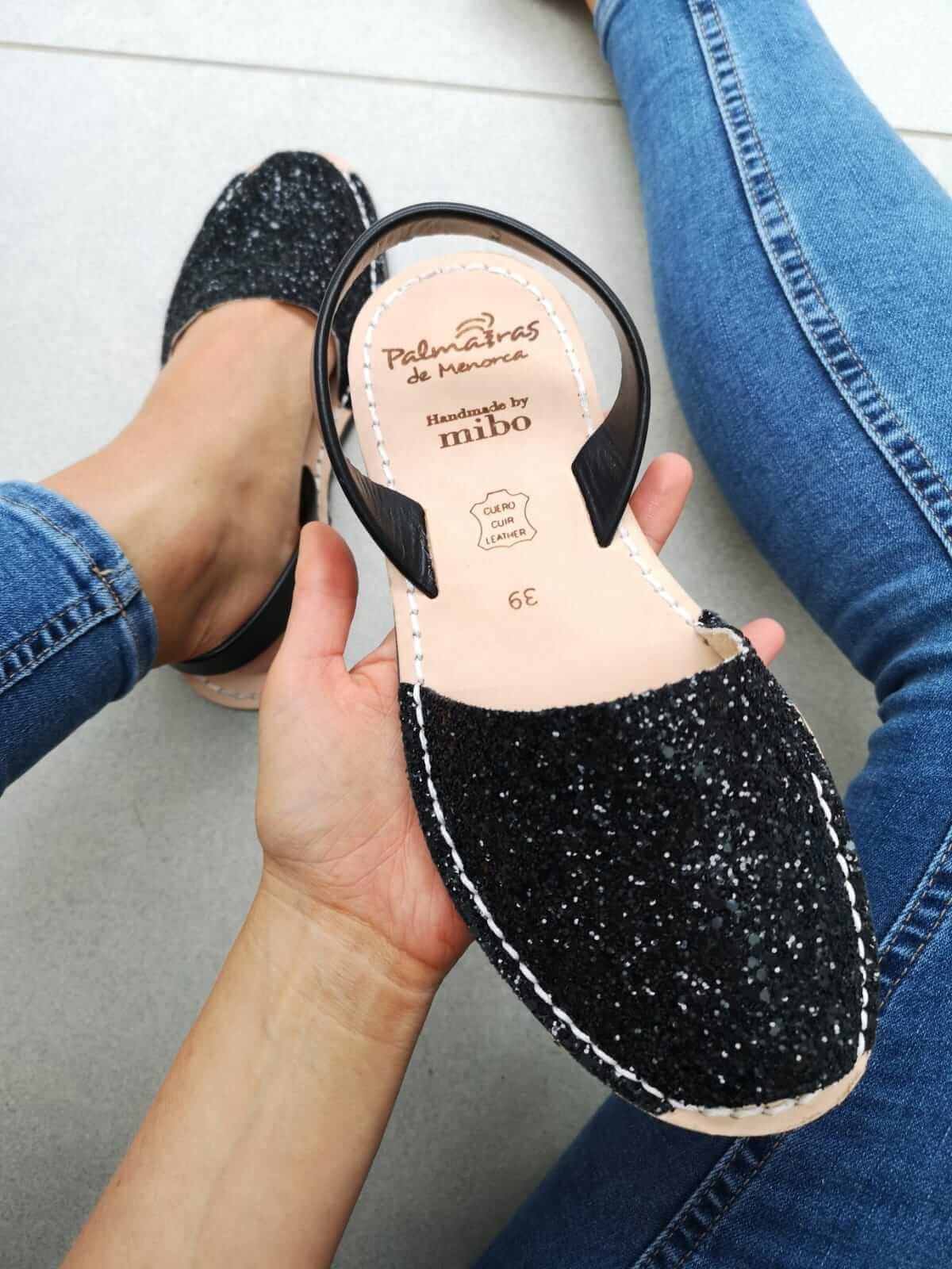 Black glittery sandal held by a hand with a white background