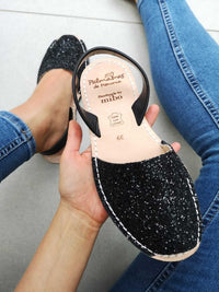 Black glittery sandal held by a hand with a white background