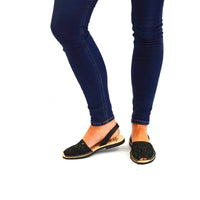 Person wearing dark blue jeans and black open-toe shoes on a white background