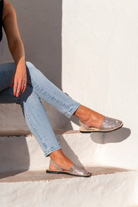 A person seated on white outdoor steps wearing light blue jeans and glitter slingback sandals with black soles, against a white stucco wall.