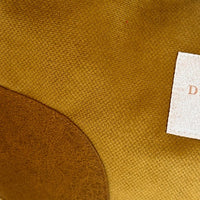 Close-up of olive woven fabric surface with a curved darker brown patch and a small white fabric tag showing part of a letter.