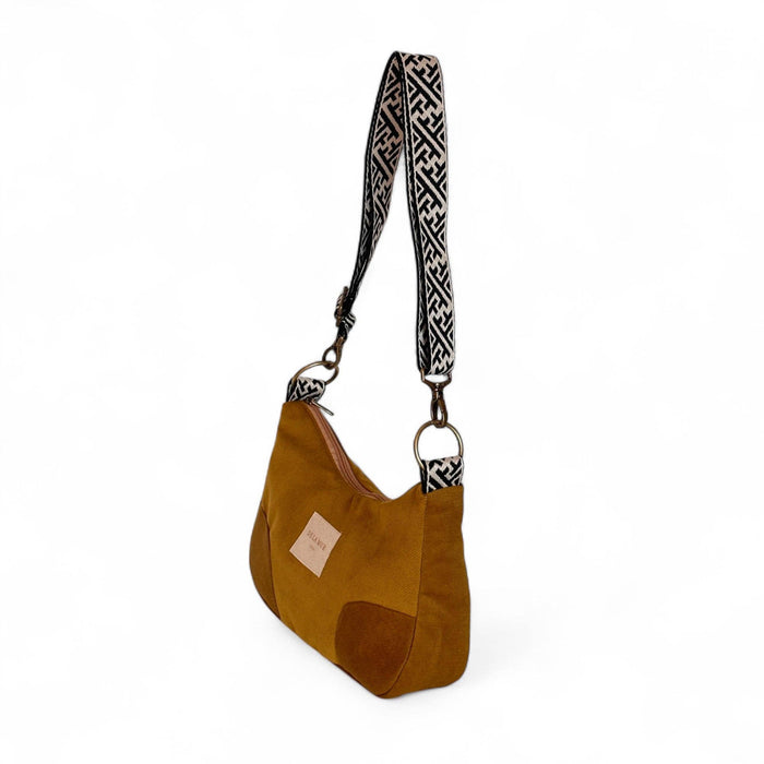 A olive suede shoulder bag with a black and white patterned woven strap, shown on a clean white background.