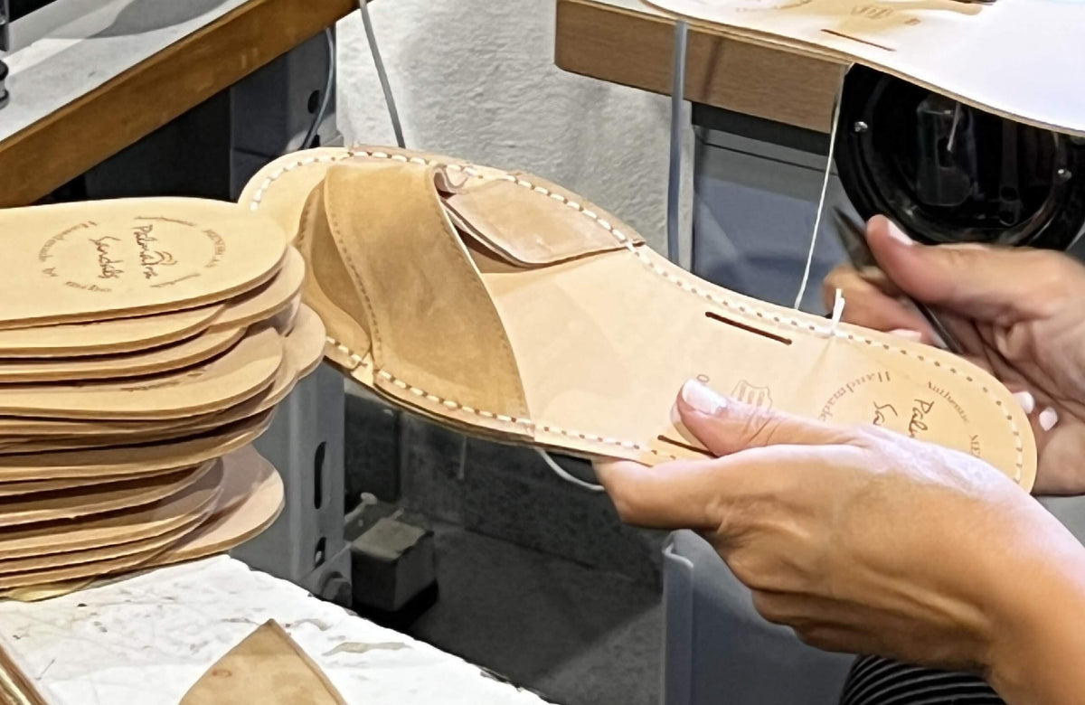Close-up of a person holding a leather shoe insole with stacks of similar insoles on a table.