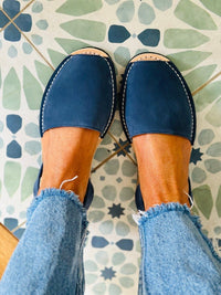 Blue sandals worn with light blue jeans on a patterned floor.