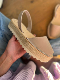 Taupe sandal with a textured sole held by a person wearing jeans and a sweater.