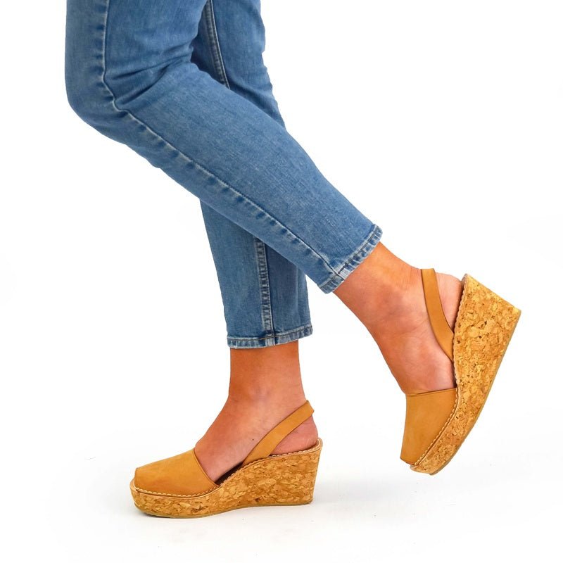 Tan wedge sandals worn with blue jeans on a white background