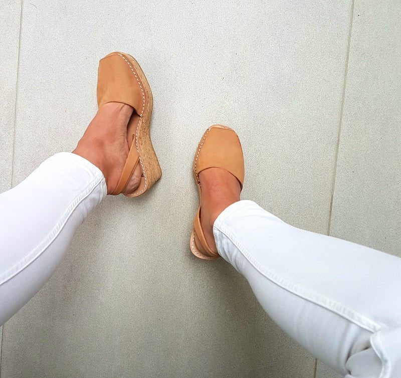 Tan wedges worn with white pants on a light grey floor.