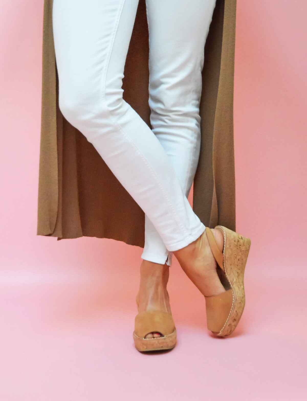 Person wearing white jeans and tan wedges on a pink background