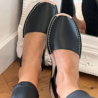 Black leather sandals worn indoors on a wooden floor.