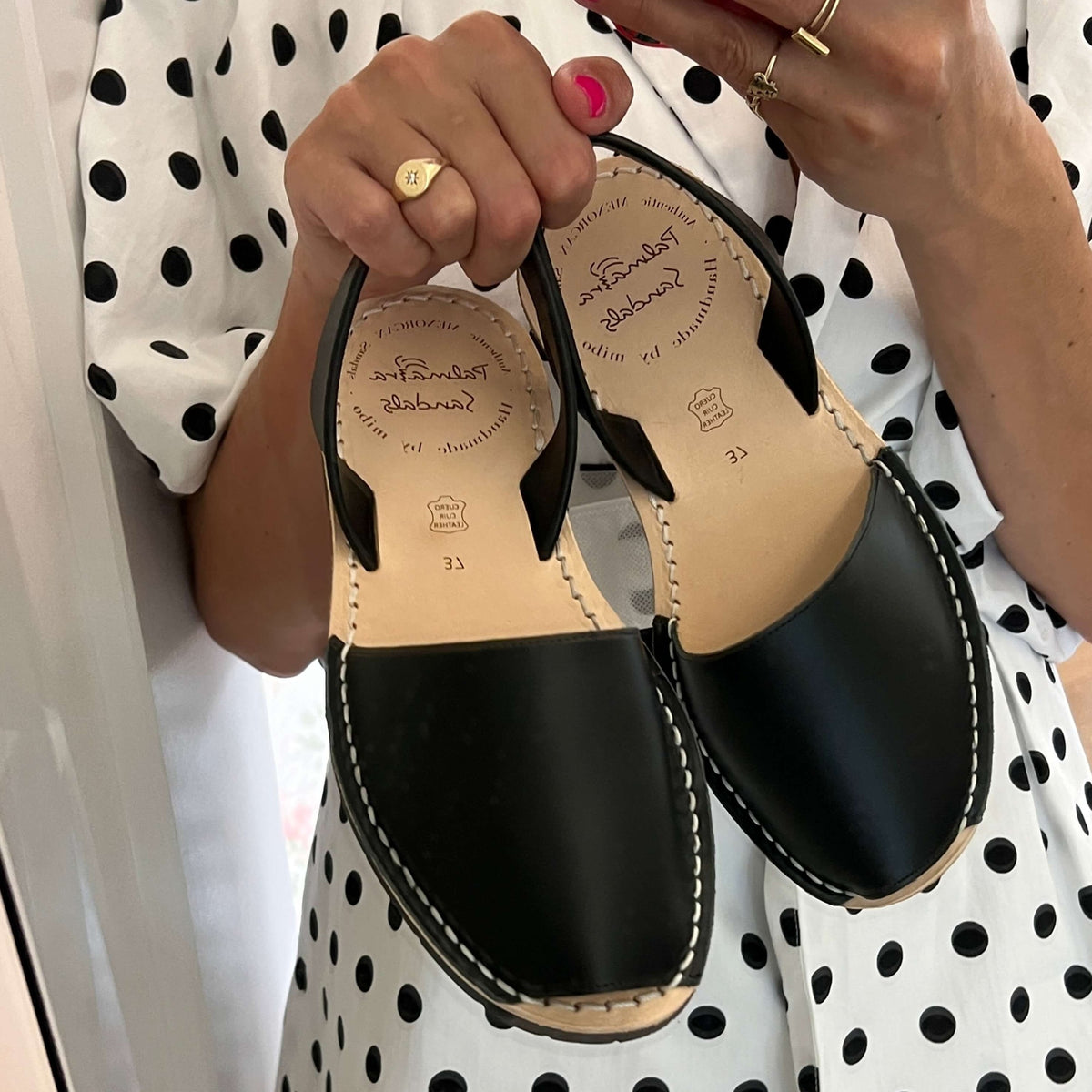 Black sandals held by a person wearing a polka dot dress.