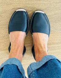 black leather avarcas worn with blue jeans on a wooden floor.