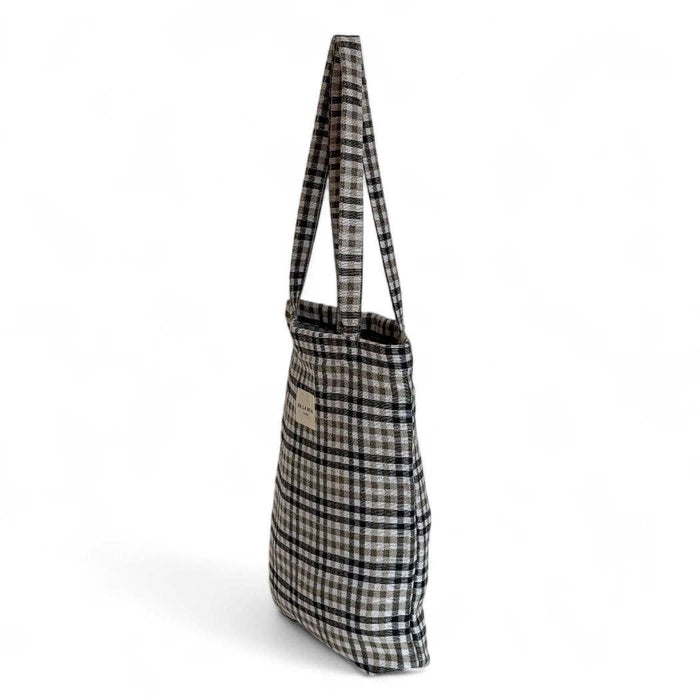 A plaid shoulder bag in black, white, and beige, shown from a side profile view against a plain white background.