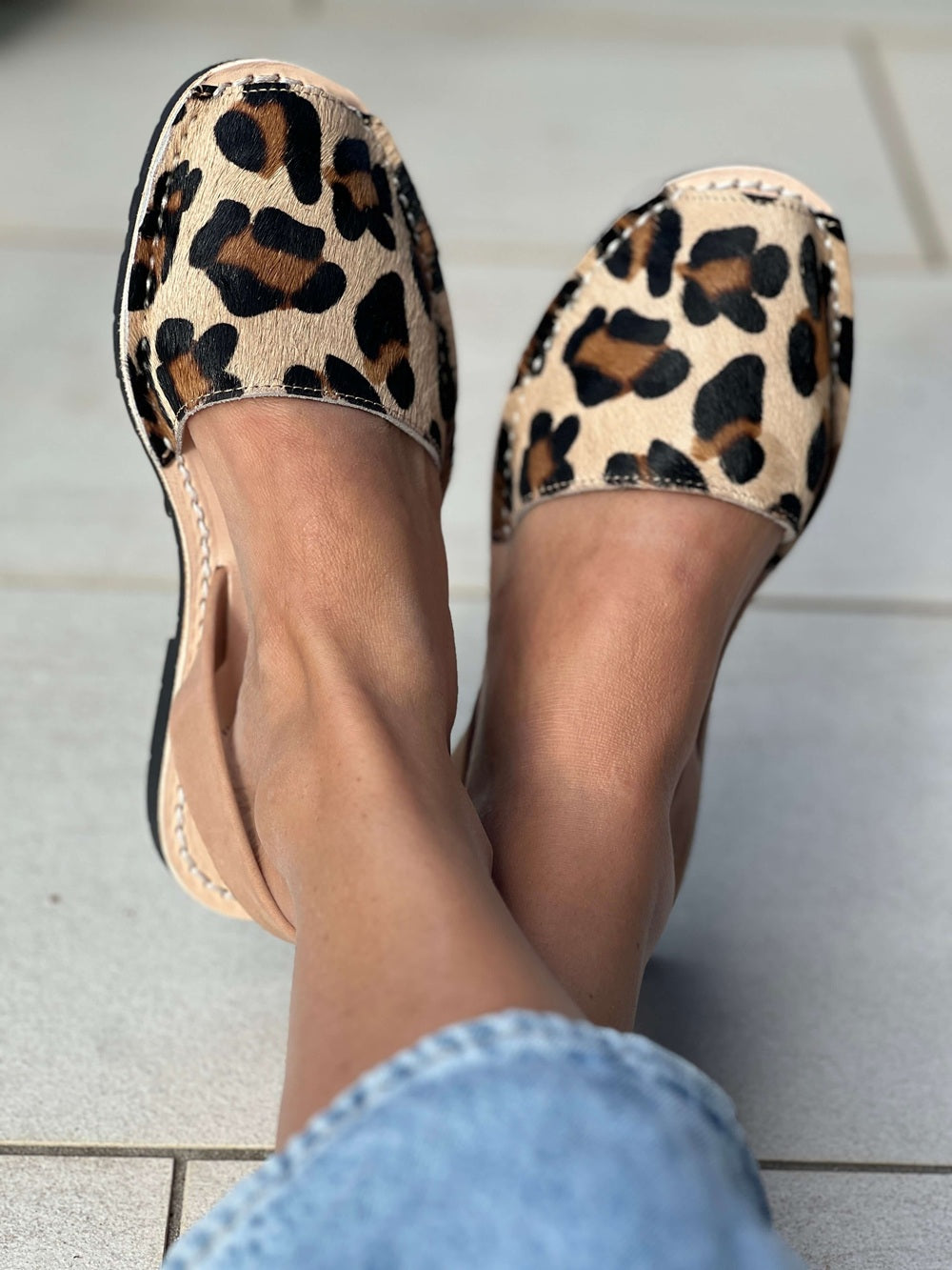 Leopard print sandals worn on a light grey tiled floor.