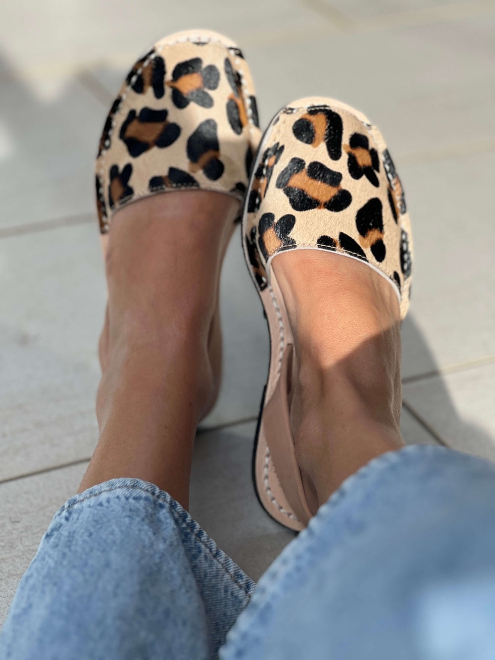 Leopard print flats worn with light blue jeans on a light background