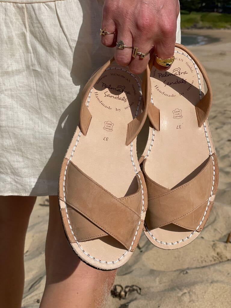 georgia tan sandals with visible brand name held by a person on a beach.