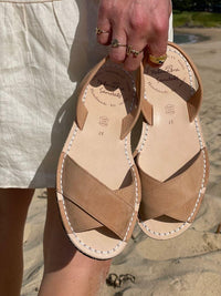 georgia tan sandals with visible brand name held by a person on a beach.