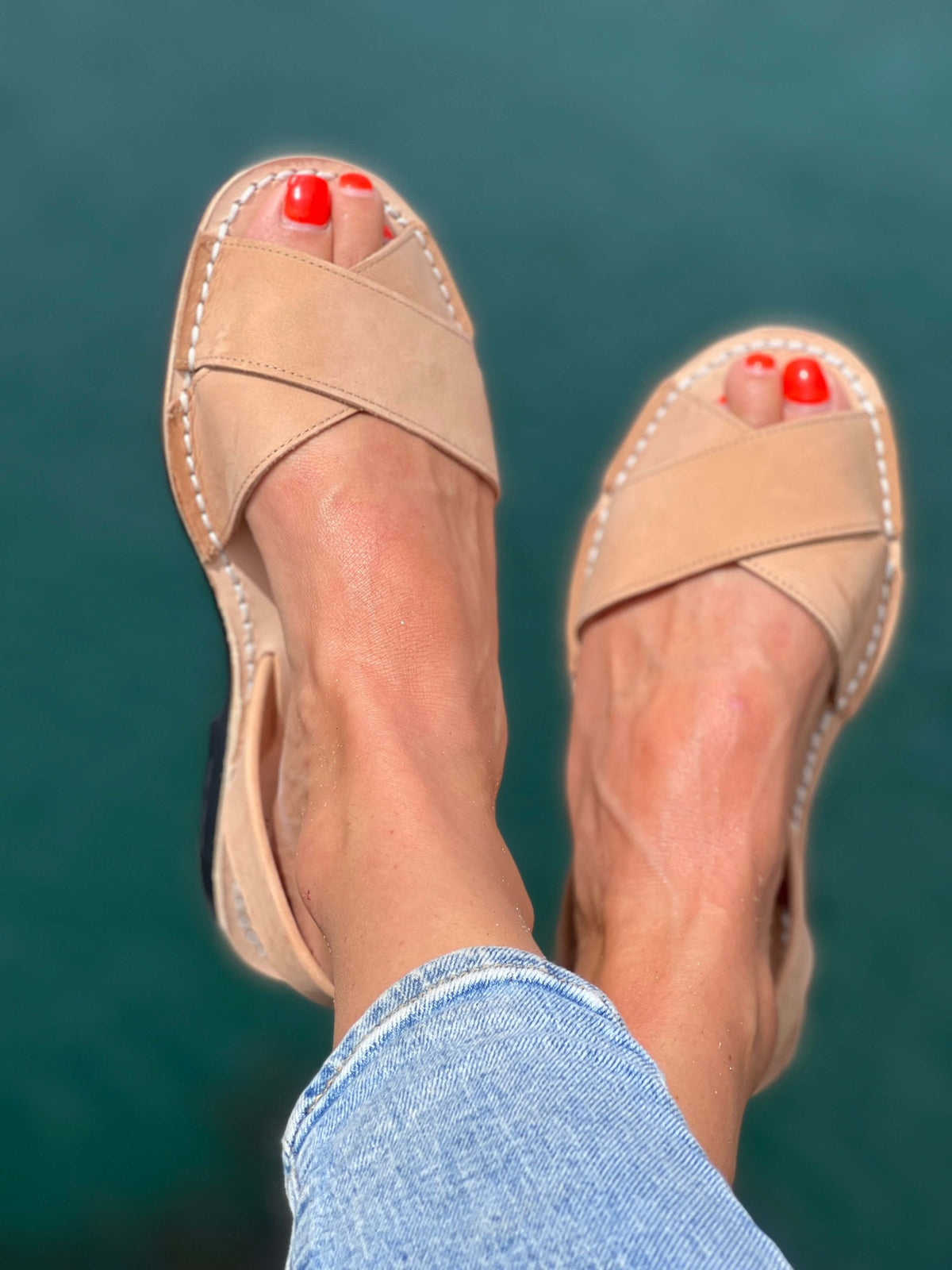 Tan sandals worn with blue jeans against a teal background