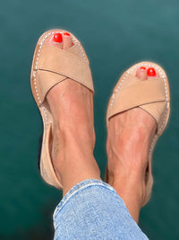 Tan sandals worn with blue jeans against a teal background