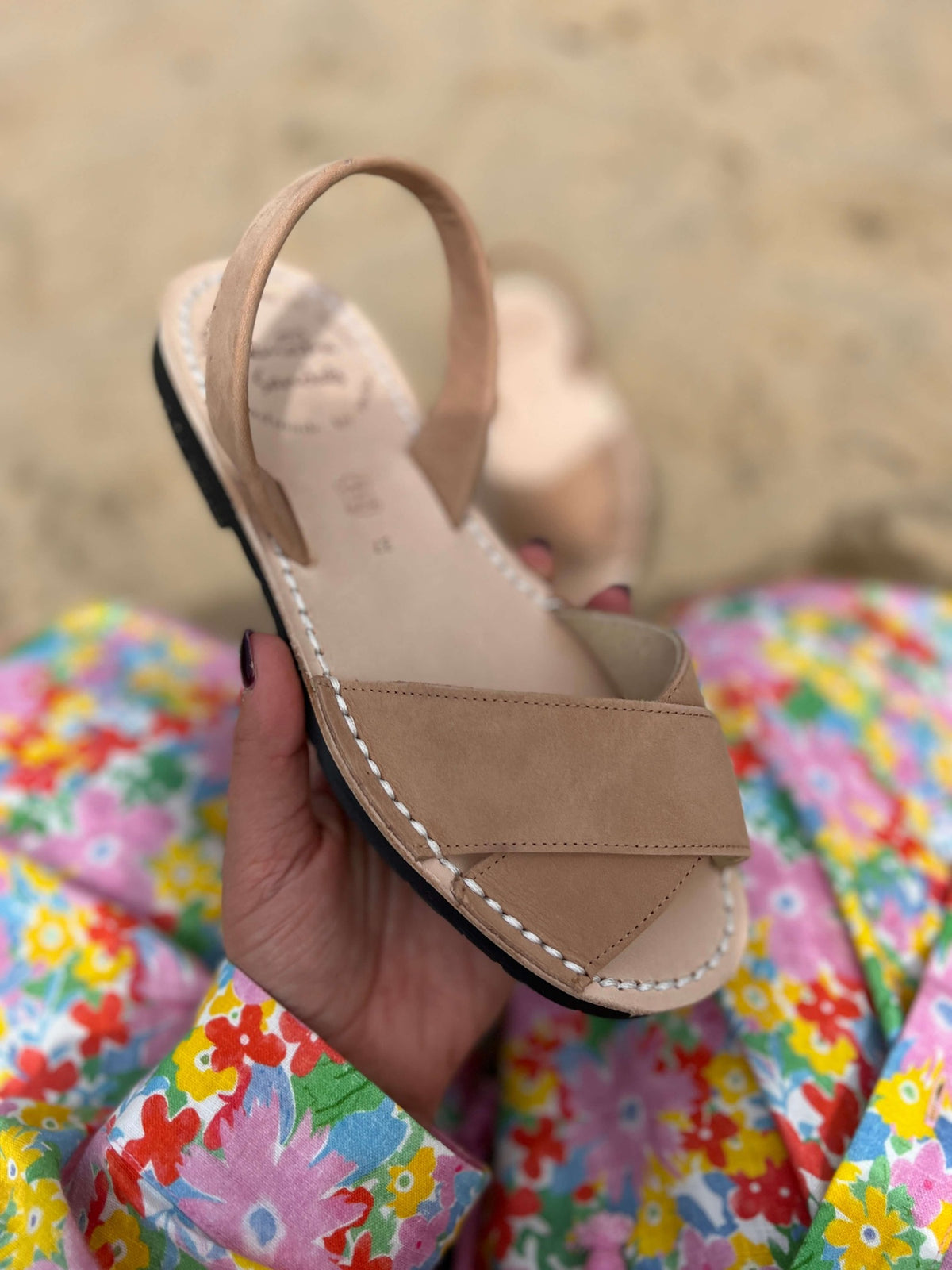Georgia tan sandal held by a hand with a colorful floral background