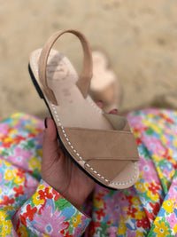 Georgia tan sandal held by a hand with a colorful floral background