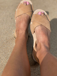Tan sandals worn on feet with pink nail polish on a sandy surface