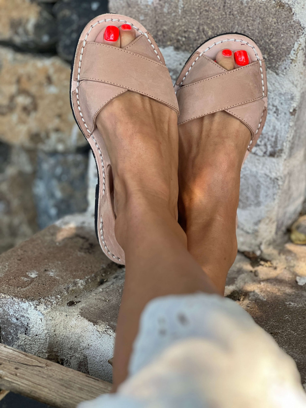 Tan sandals worn on feet with red nail polish, sitting on a stone surface.