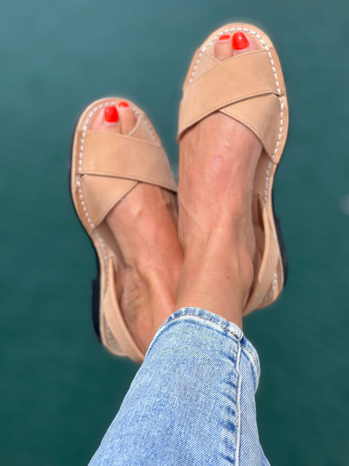 Tan sandals worn with blue jeans against a teal background