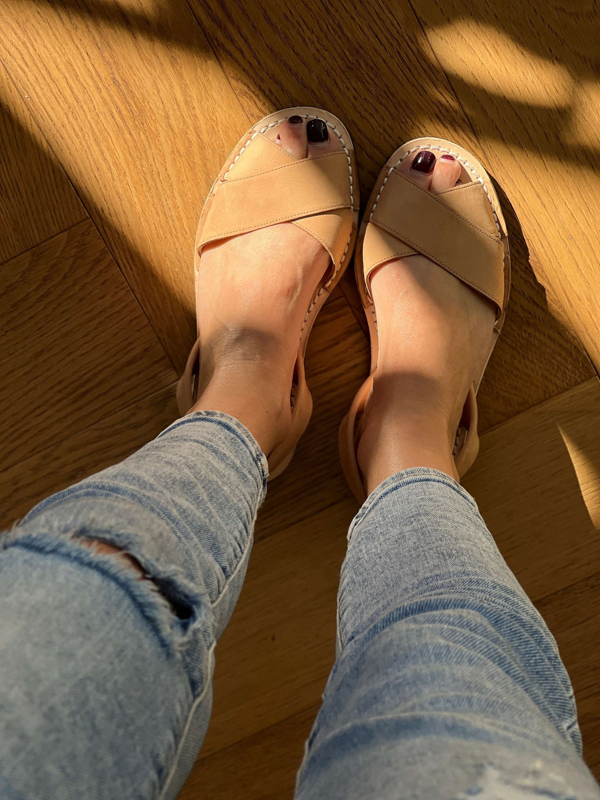 Tan sandals worn with light blue jeans on a wooden floor.