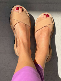 tan sandals worn on feet with red nail polish against a grey background