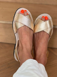 Gold sandals worn on feet with orange nail polish against a wooden floor background