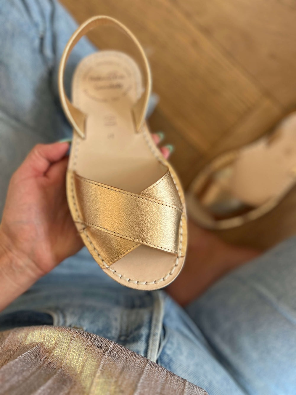 Gold sandal held by a hand with a wooden floor background