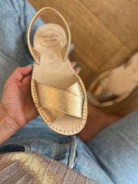 Gold sandal held by a hand with a wooden floor background