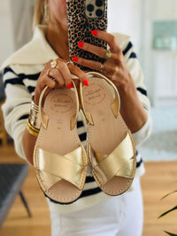 Gold sandals held by a person with a blurred background