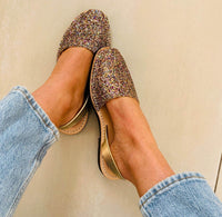 Gold glittery avarcas worn with light blue jeans on a neutral background