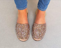 Glittery gold shoes worn with blue jeans on a neutral background