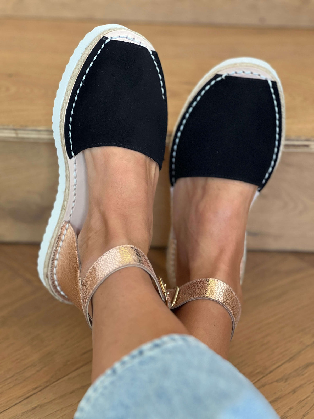 Black espadrilles with gold straps worn on a wooden floor