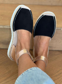 Black espadrilles with gold straps worn on a wooden floor