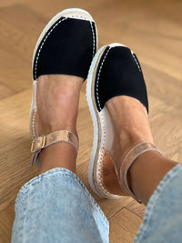 Black and white shoes worn with light blue jeans on a wooden floor.
