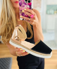 Black sandal with rose gold sole held by a person.