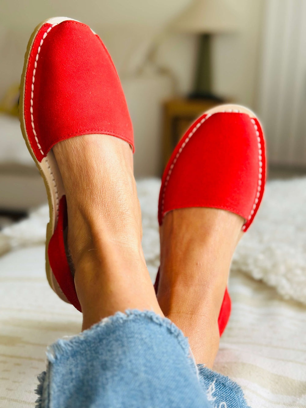 Red avarcas worn with denim jeans on a blurred indoor background