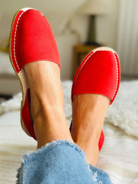 Red avarcas worn with denim jeans on a blurred indoor background