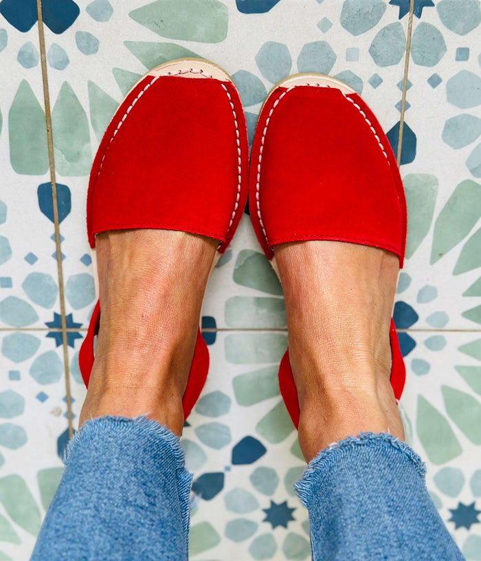 Red slip-on shoes worn with blue jeans on a patterned tile floor.