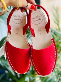 Red sandals with branding held by a hand against a blurred green background.