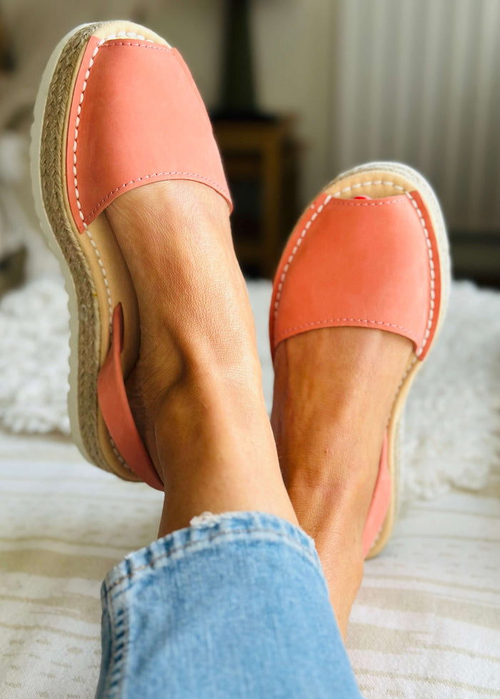 Peach espadrilles worn with blue jeans on a neutral background