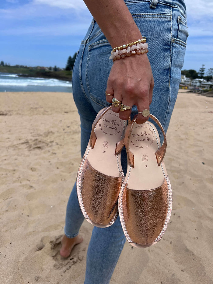 Person holding a pair of sandals on a beach with ocean background