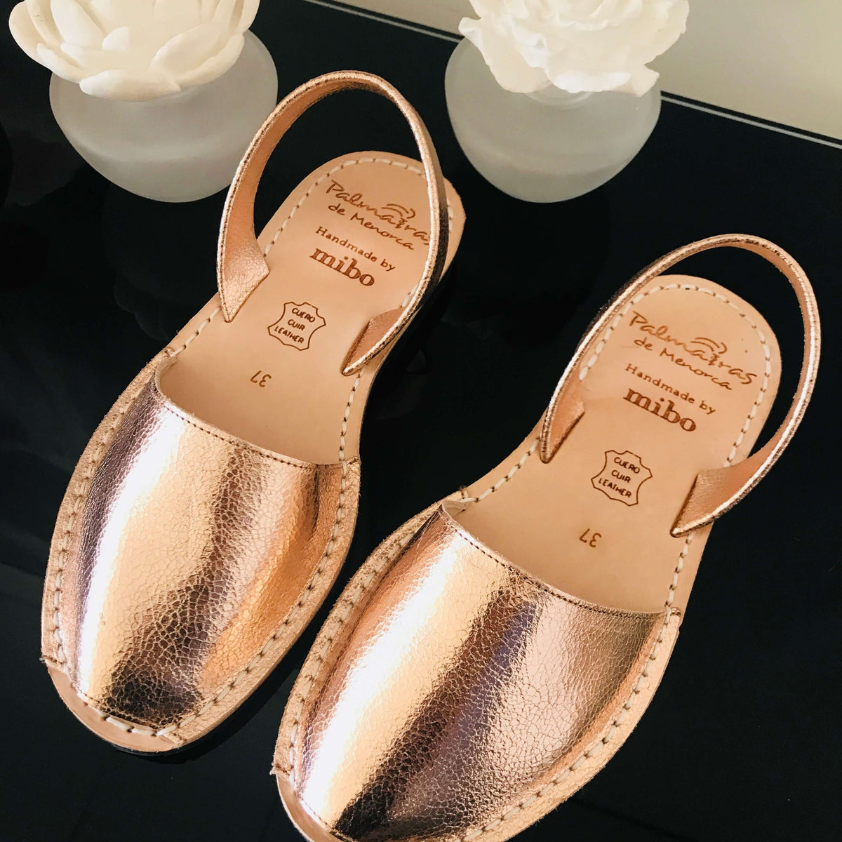 Pair of rose gold sandals with brand name on a dark background