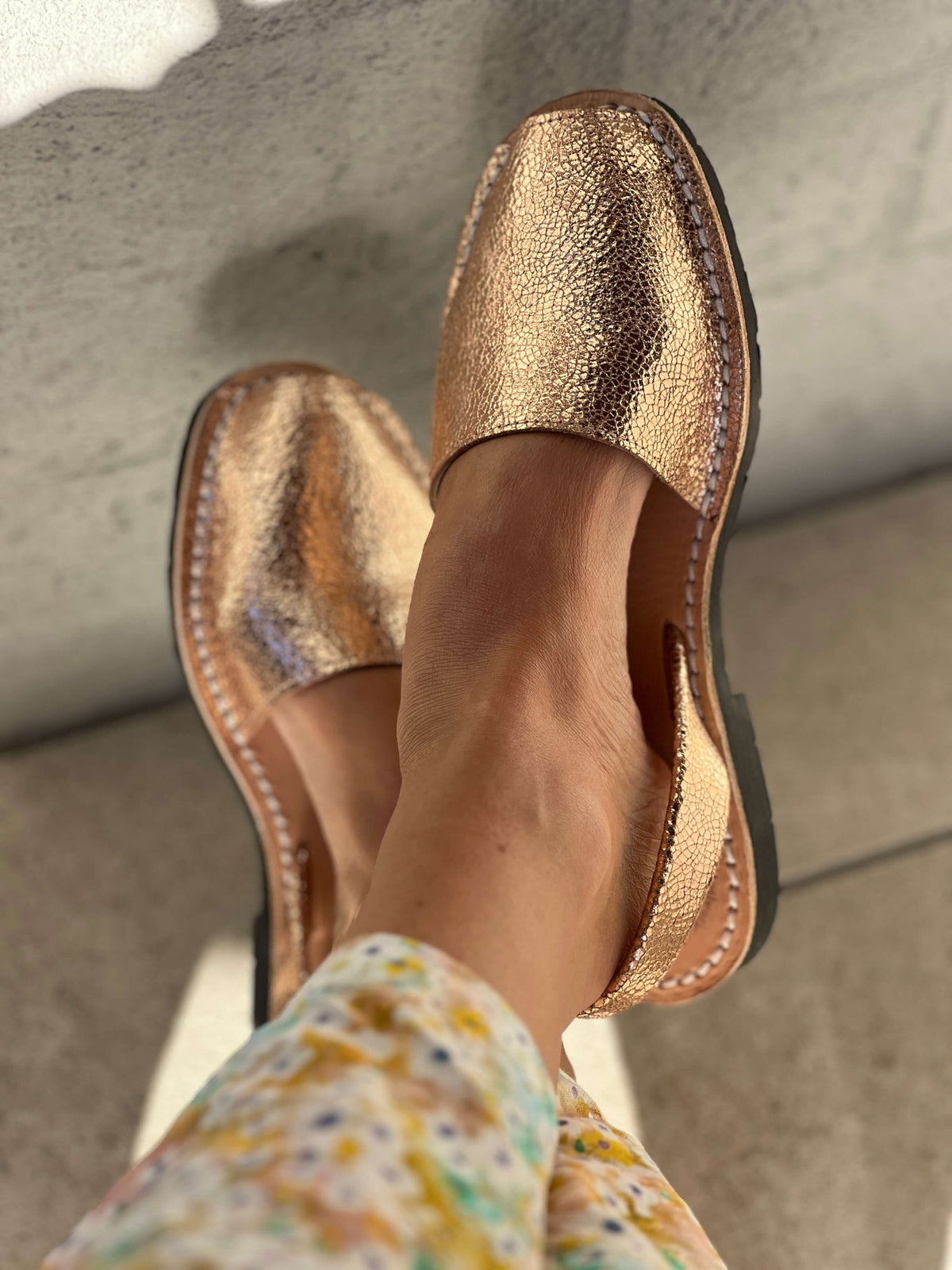 Gold metallic sandals worn with a floral dress on a neutral background