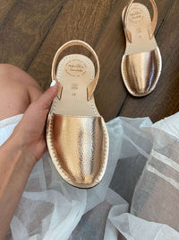 Rose gold sandals held by a hand on a wooden floor