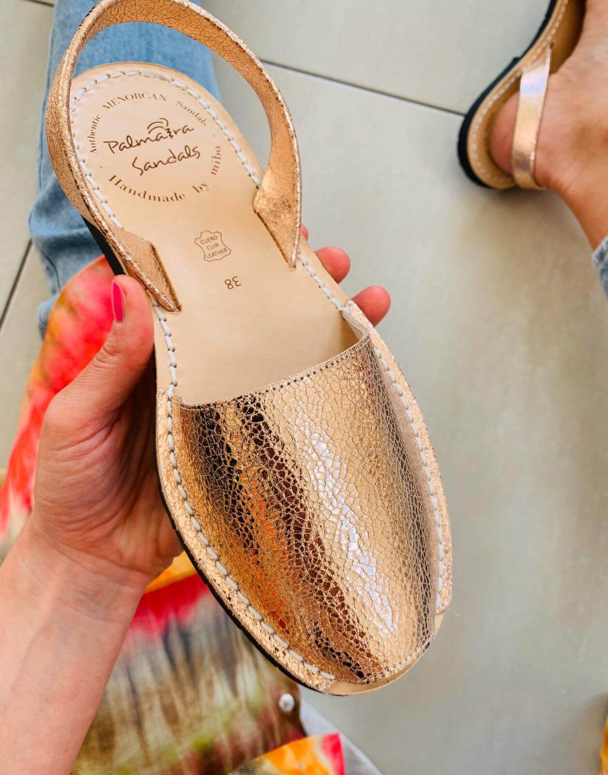 Rose Gold sandal with 'Palmaira Sandals' branding held by a person.