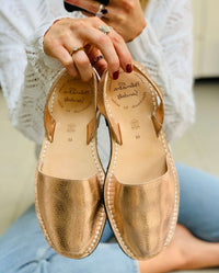 Rose Gold sandals held by a person wearing a white sweater and blue jeans.